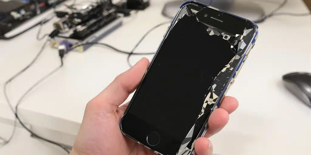 Damaged iPhone with cables near a computer on table