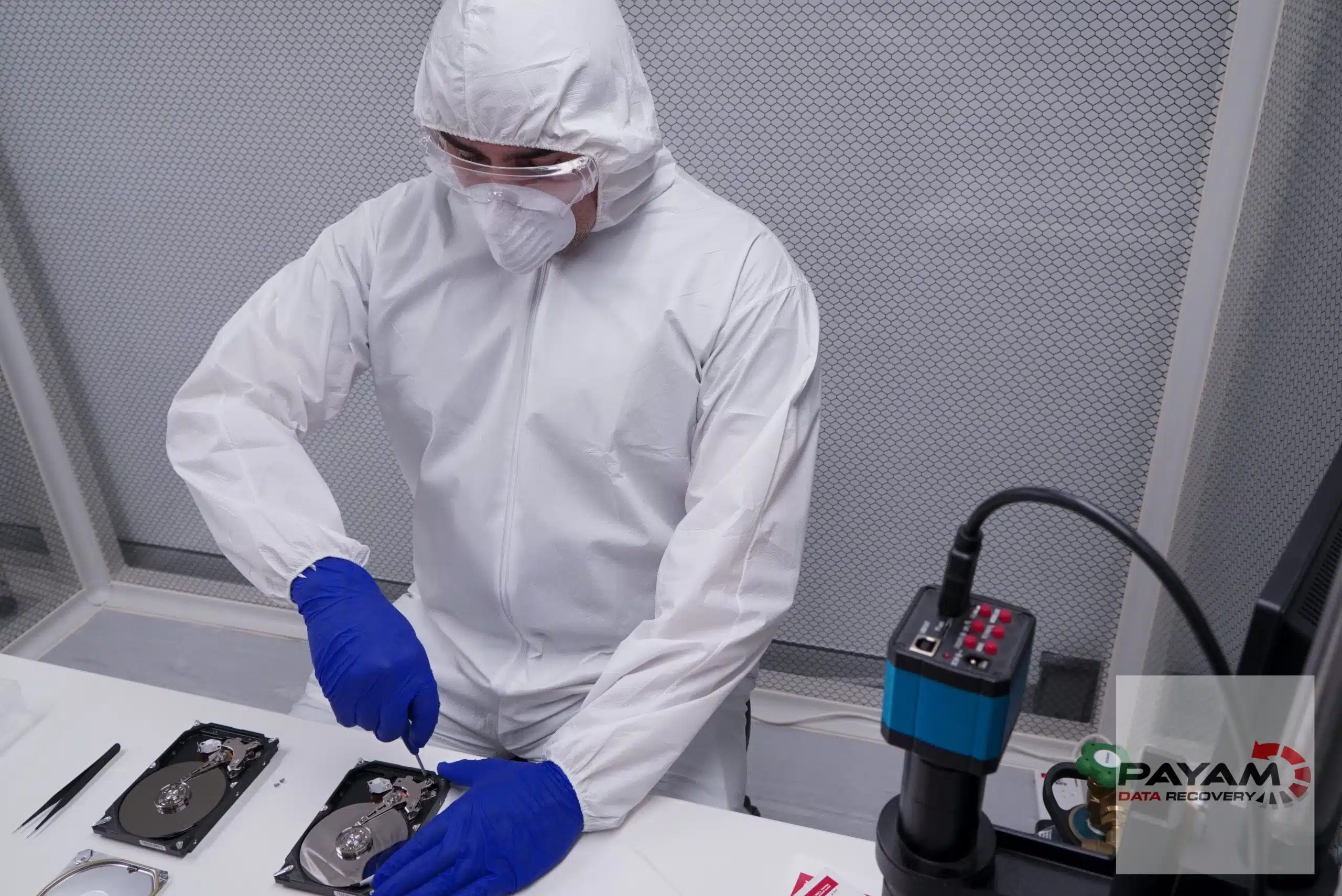 Technician in a full cleanroom suit working on a small hard drive in the laminar flow cabinet