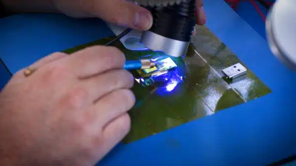 Technician using a UV curing lamp on a circuit board with soldered wires